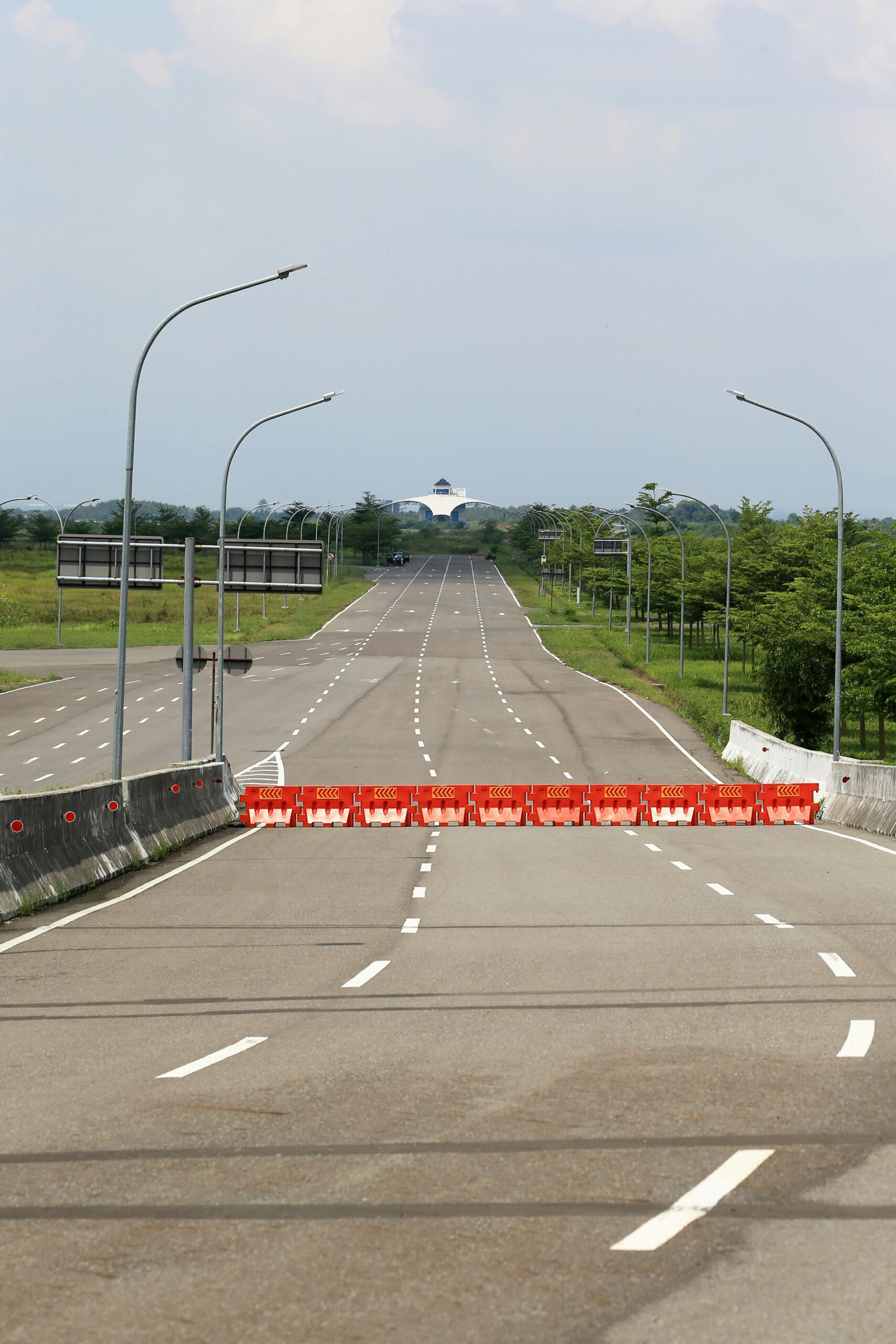 Empty highway blocked by orange barricades with distant building under blue sky.