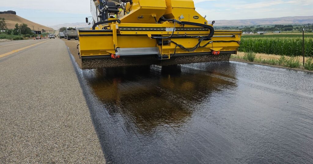 Yellow road construction machine applying asphalt on a rural road in Marsing, Idaho.